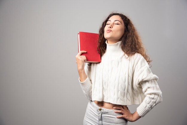 灰色の壁に赤い本を持っている若い女性。高品質の写真