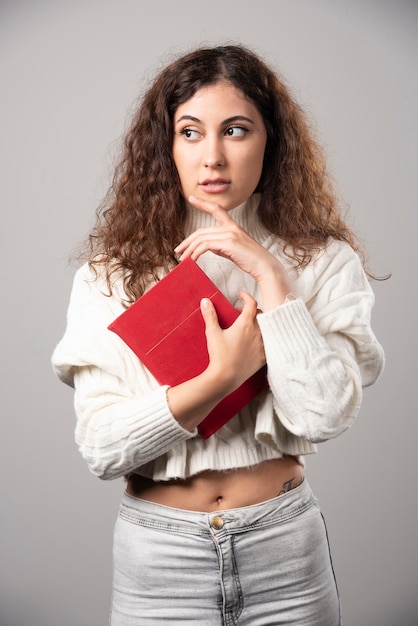 Young woman holding red book on a gray wall. High quality photo