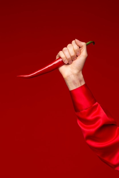 Young woman holding red chili pepper as knife