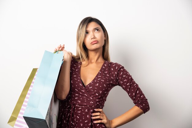 Young woman holding shop bags on white wall.