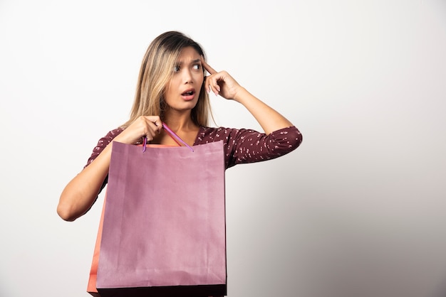 Young woman holding shop bags on white wall.