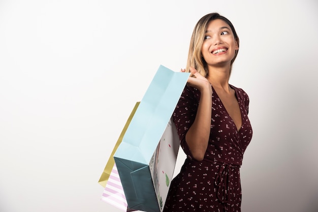 Young woman holding shop bags on white wall. 