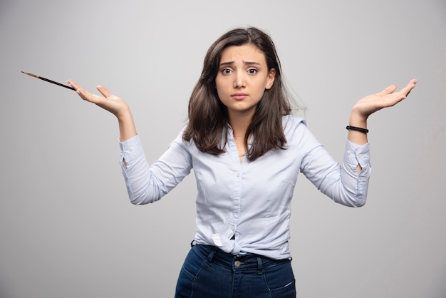 Free photo young woman holding single brush on gray wall. high quality illustration