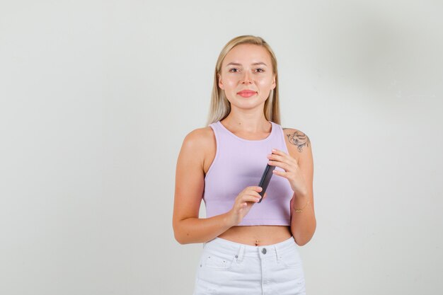 Young woman holding smartphone and smiling in singlet