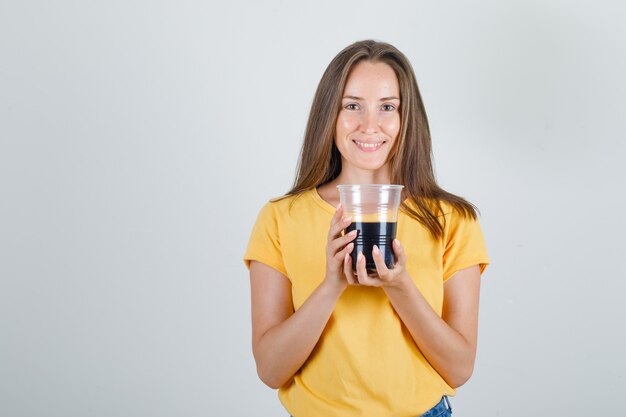 Young woman holding soft drink in cup in t-shirt, shorts and looking cheerful