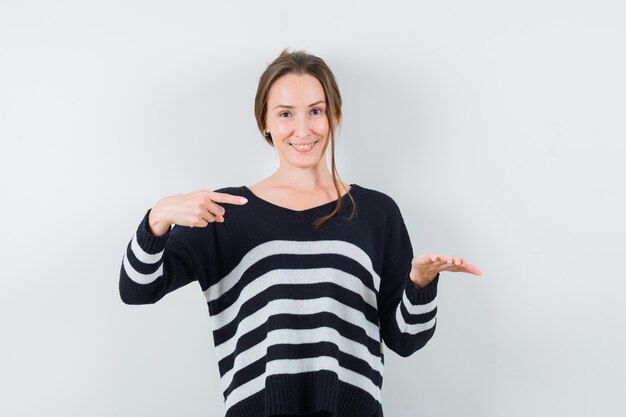 Young woman holding something on hand imaginary and pointing to it in black blouse and black pants and looking happy