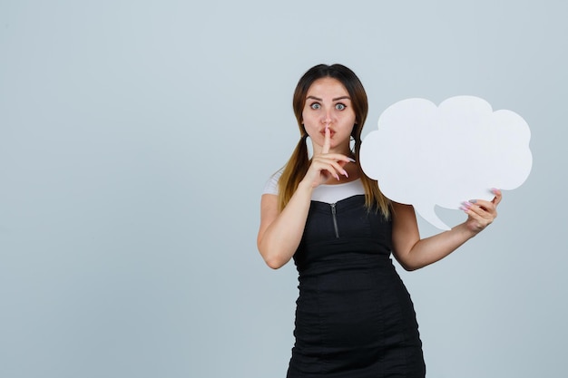 Free photo young woman holding speech bubble while showing silence gesture