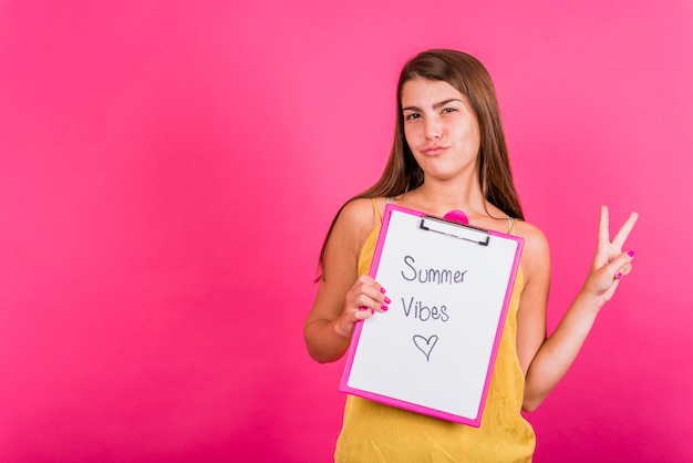 Young woman holding tablet with paper on pink background