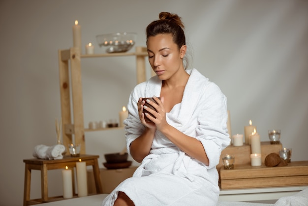 Young woman holding tea cup relaxing in spa salon.