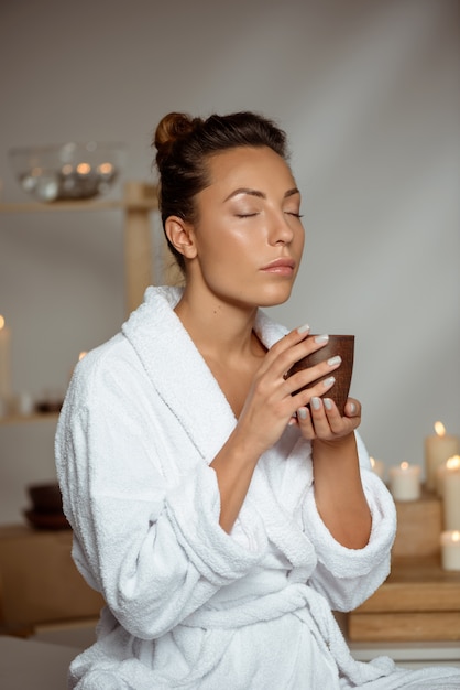 Young woman holding tea cup relaxing in spa salon.