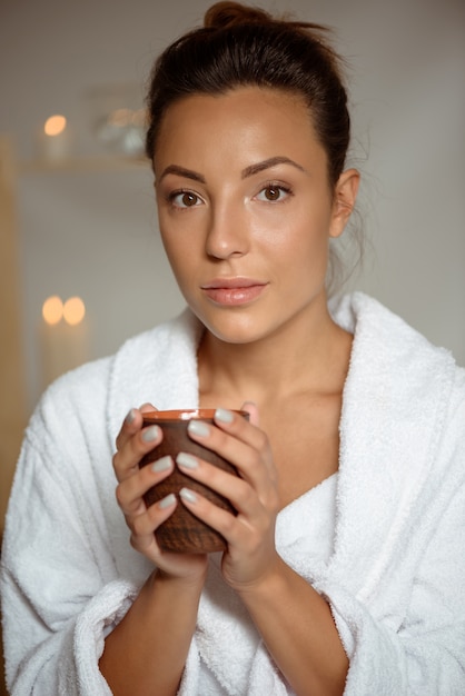 Free photo young woman holding tea cup relaxing in spa salon.