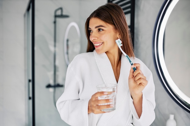 Young woman holding a toothbrush and a glass of water