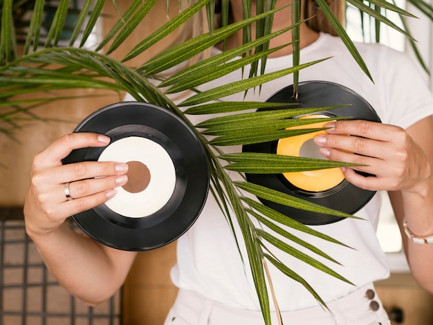Young woman holding vinyl records in both hands behind plant
