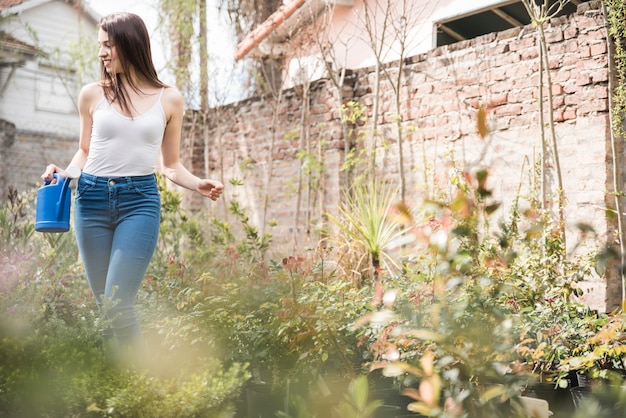 Latta di innaffiatura della holding della giovane donna che si leva in piedi fra le piante crescenti