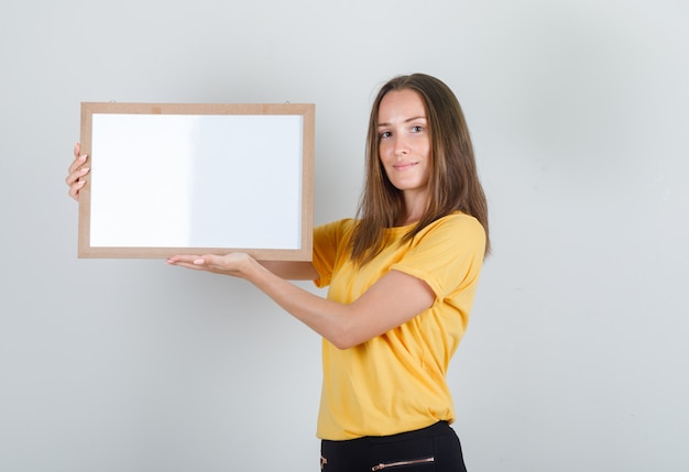 ホワイトボードを保持し、黄色のTシャツで笑っている若い女性