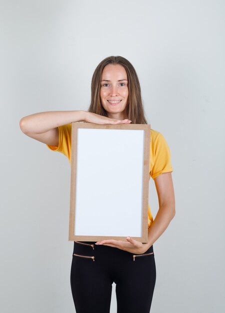 Молодая женщина держит белую доску и улыбается в желтой футболке