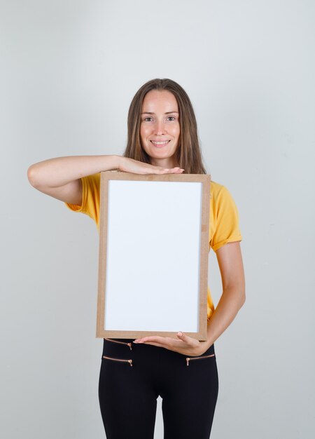 Young woman holding white board and smiling in yellow t-shirt