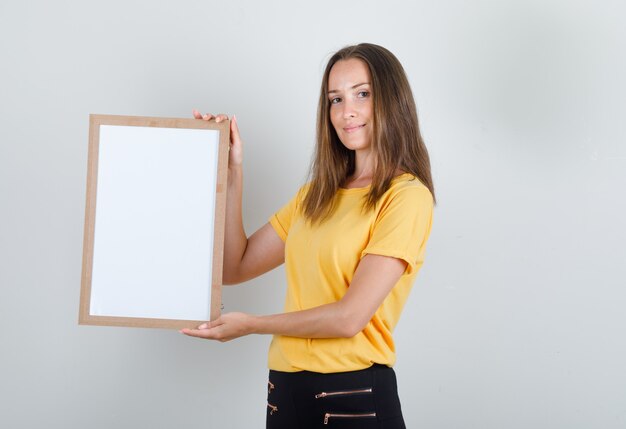 Young woman holding white board and smiling in yellow t-shirt