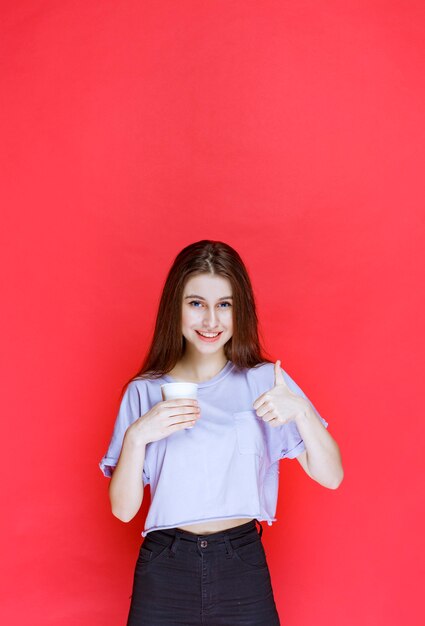 young woman holding a white disposable water cup and showing satisfaction sign.