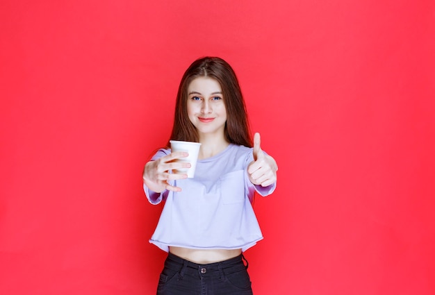 young woman holding a white disposable water cup and showing satisfaction sign.