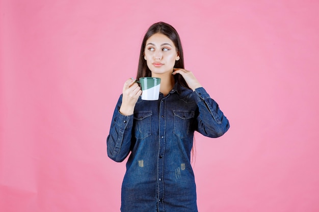 Young woman holding a white green coffee mug and smelling