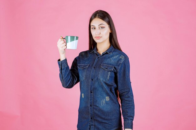 Young woman holding a white green coffee mug and smelling