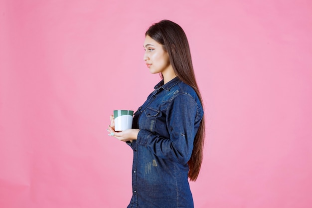 Young woman holding a white green coffee mug and smelling