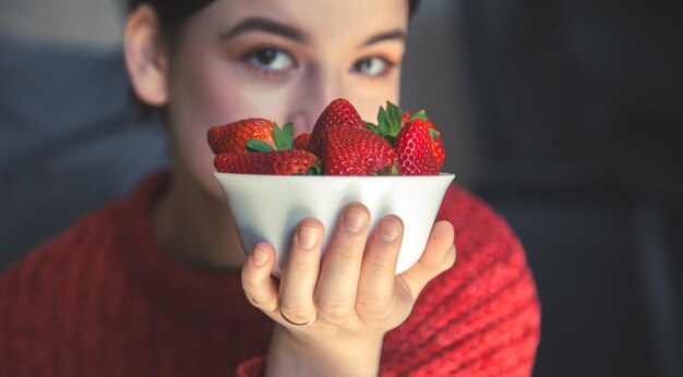 若い女性は彼女の手にイチゴのボウルを持っています