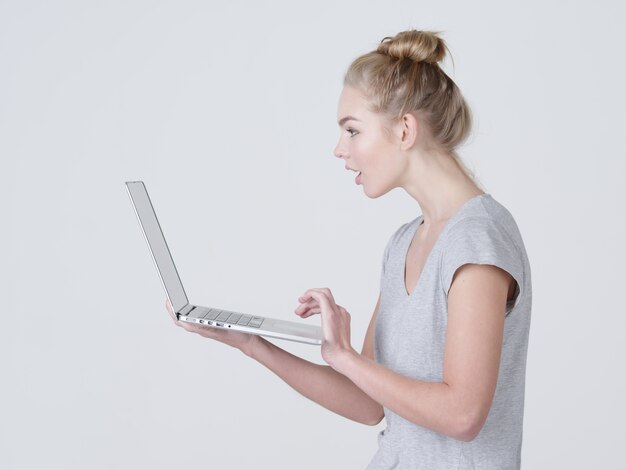 Молодая женщина держит ноутбук в habds. Шокированная кавказская девушка с ноутбуком позирует в студии