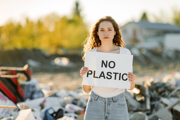 Free photo a young woman  holds a poster. the inscription no plastic. showing a sign protesting against plastic pollution.