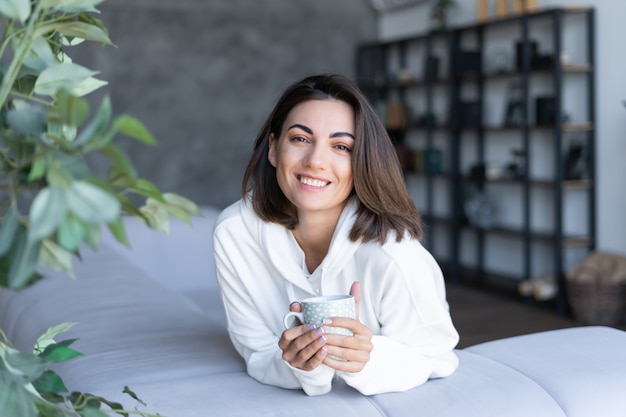 Foto gratuita una giovane donna a casa con una felpa con cappuccio bianca sul divano si siede pacificamente, gode della solitudine