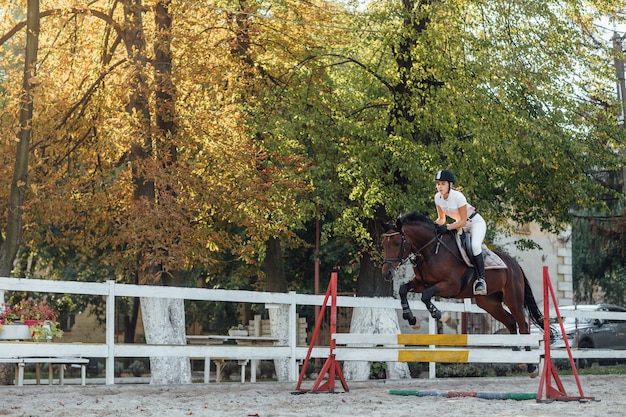 Молодая женщина-всадник-спортсменка на соревнованиях по конному спорту, перепрыгивая через препятствие