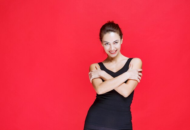 Бесплатное фото Молодая женщина в черной майке, стоящей на красной стене