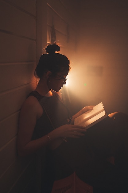 Бесплатное фото Молодая женщина в очках читает книгу в уютной гостиной