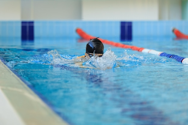 Молодая женщина в очках и кепке плавает брассом в крытом бассейне гонки.