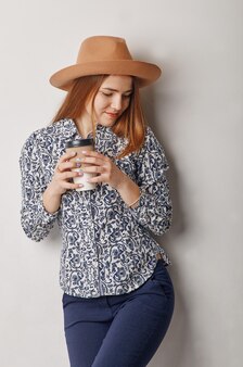 一杯のコーヒーを保持している帽子の若い女性