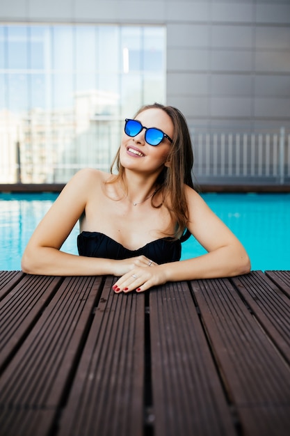 Бесплатное фото Молодая женщина в солнечных очках с идеальной белой улыбкой купается в бассейне на отдыхе