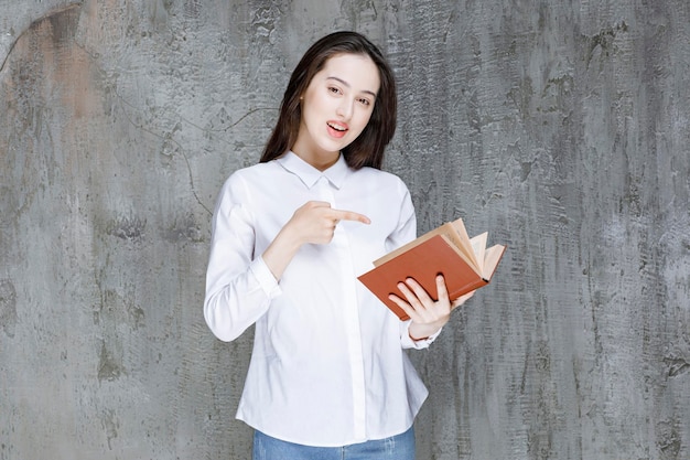 Молодая женщина в белой рубашке держит книгу для своего класса и указывает. фото высокого качества