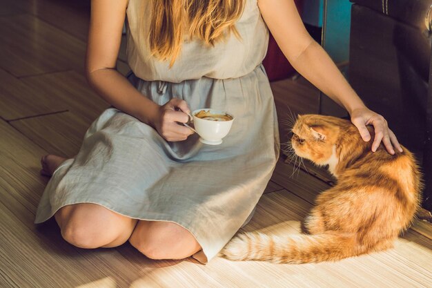 Young woman is drinking coffee and stroking the cat