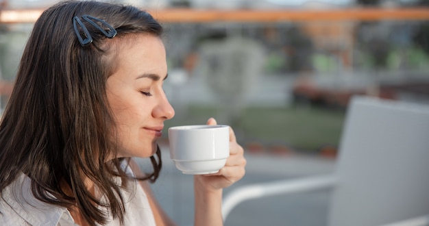 young woman is enjoying her morning coffee on an outdoor summer terrace