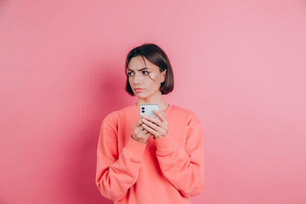 Young woman is feeling sad unhappy angry while reading sms using her mobile phone, over pink background