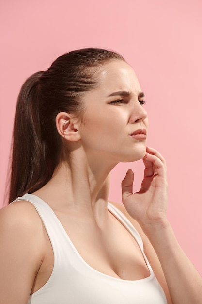 Young woman is having toothache. Pain concept. Young emotional woman. Human emotions, facial expression concept. Studio. Isolated on trendy pink color. Three-quarther view