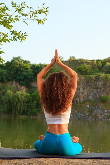 Young woman is practicing yoga near river