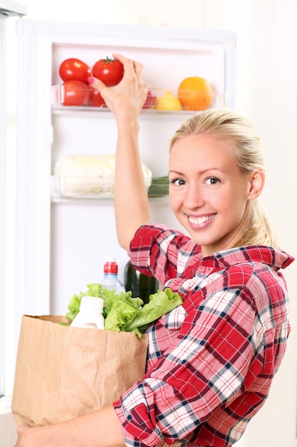 Free photo young woman is putting a food into the fridge