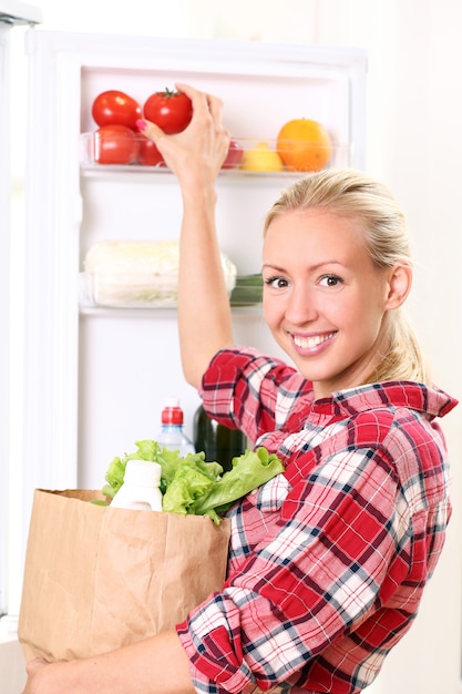 Молодая женщина кладет еду в холодильник
