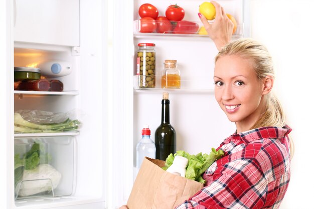 Young woman is putting a food into the fridge