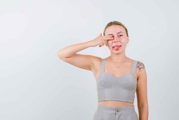 The young woman is putting hand on eye and sticking out her tongue on white background