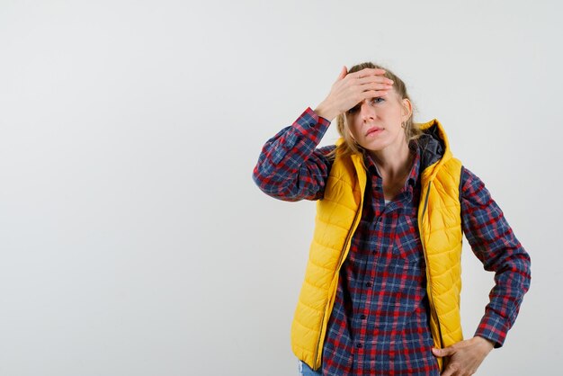 The young woman is putting her hand on forehead and putting other hand on waist  on white background