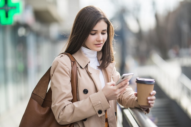 若い女性は外で彼女の電話でニュースを読んでいます。