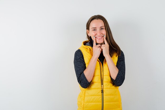 The young woman is showing her smile with forefingers on white background